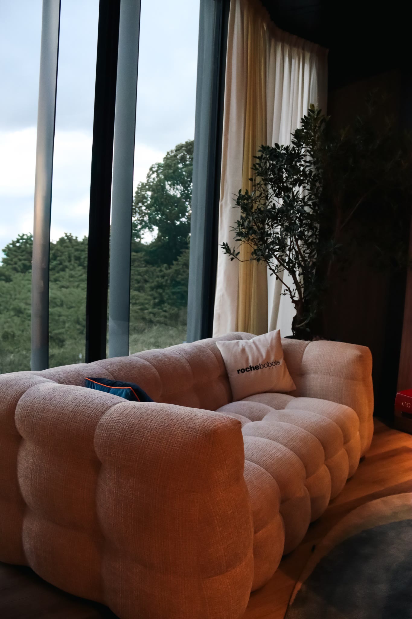 Tufted cream sofa beside a large window looking into green forest
