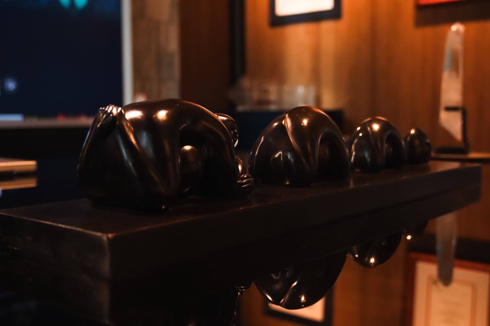 Row of dark glossy seated sculptures on a reflective surface