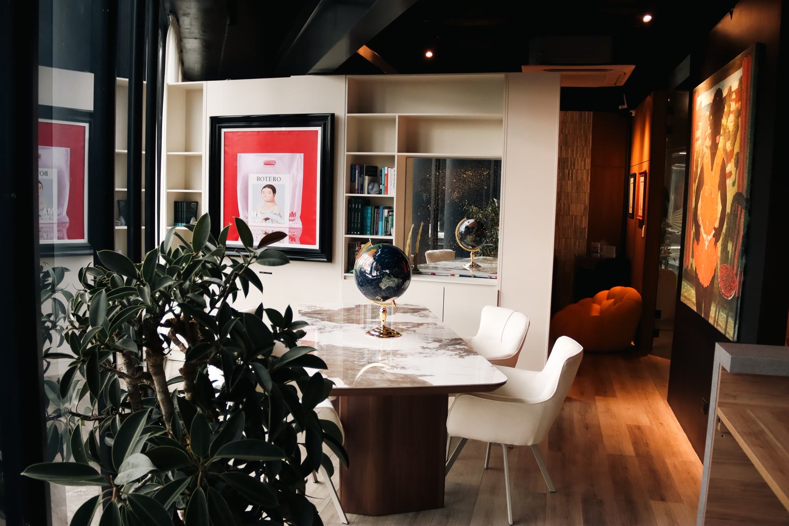Marble meeting table with a globe, two white chairs and framed works behind