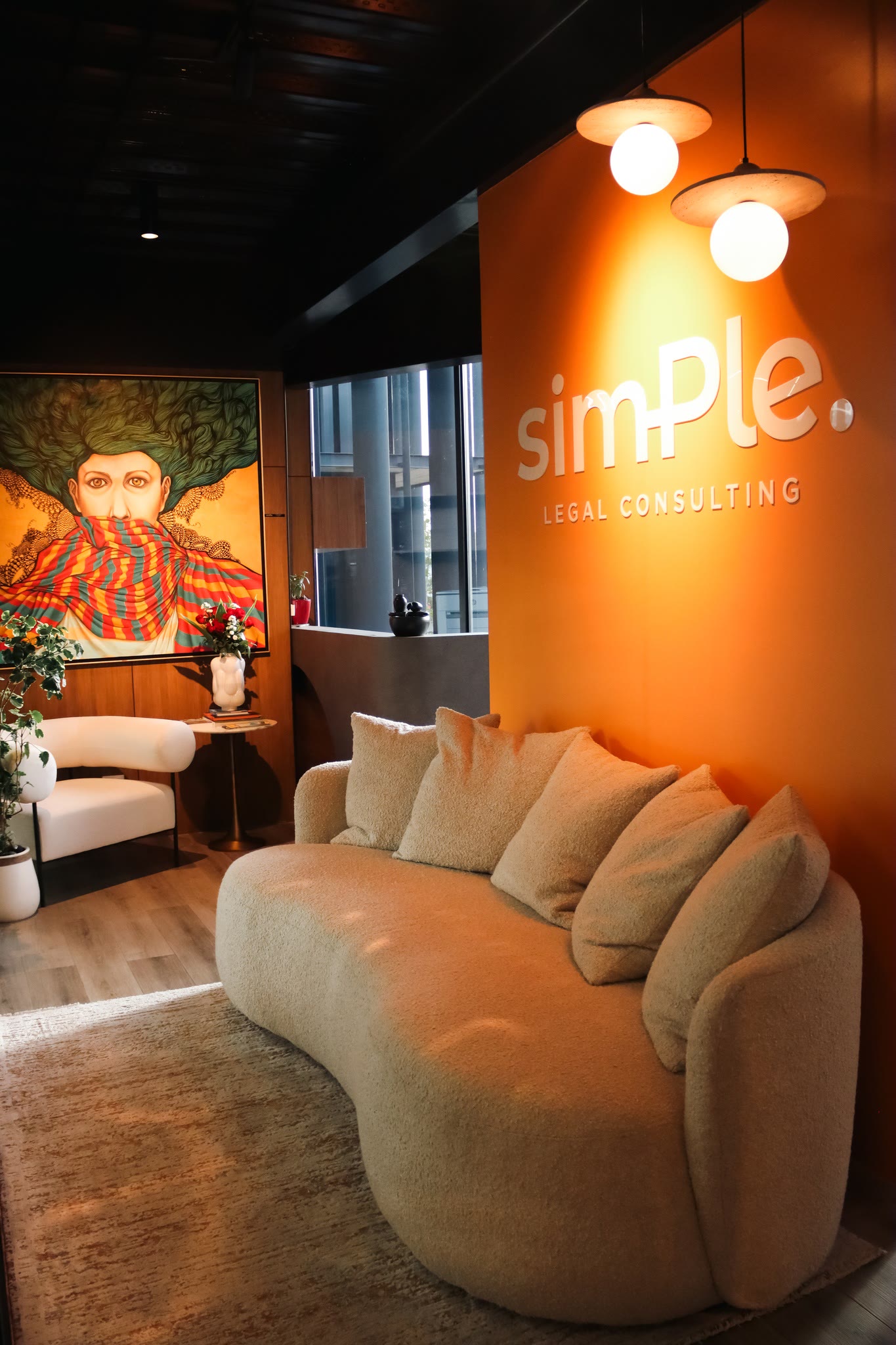 Waiting area with an orange wall carrying the firm wordmark and a large painting